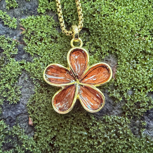 Gold flower-shaped pendant on a chain against a mossy stone background
