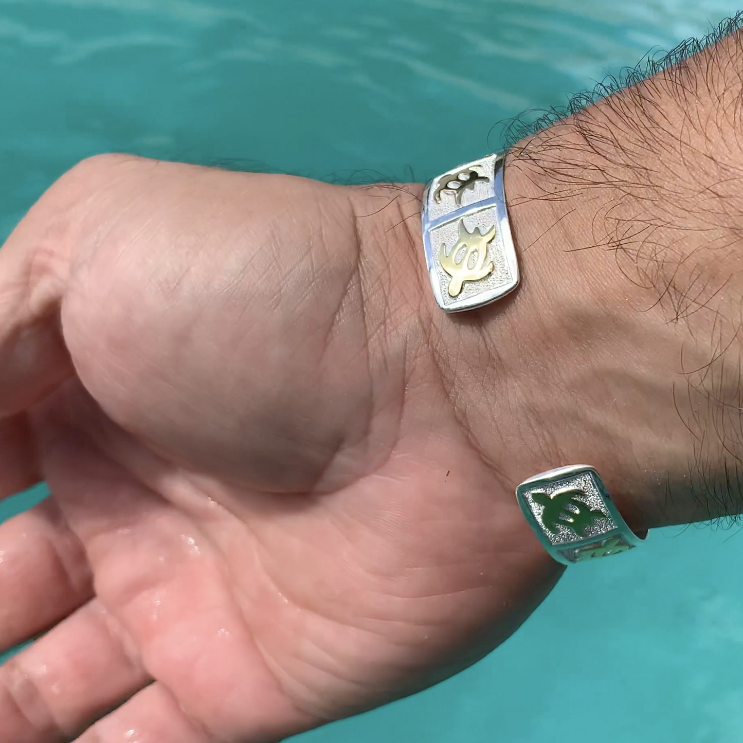 Close up of back of petroglyph honu cuff with gold honus in alternating directions on a pebble design background with a mirrored sterling silver base on model.