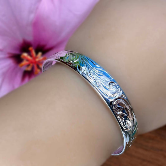 Silver bracelet on a wrist with a blurred pink flower in the background