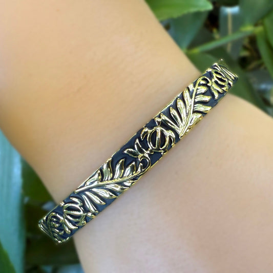 Gold bracelet with leaf pattern on a wrist against a green leafy background