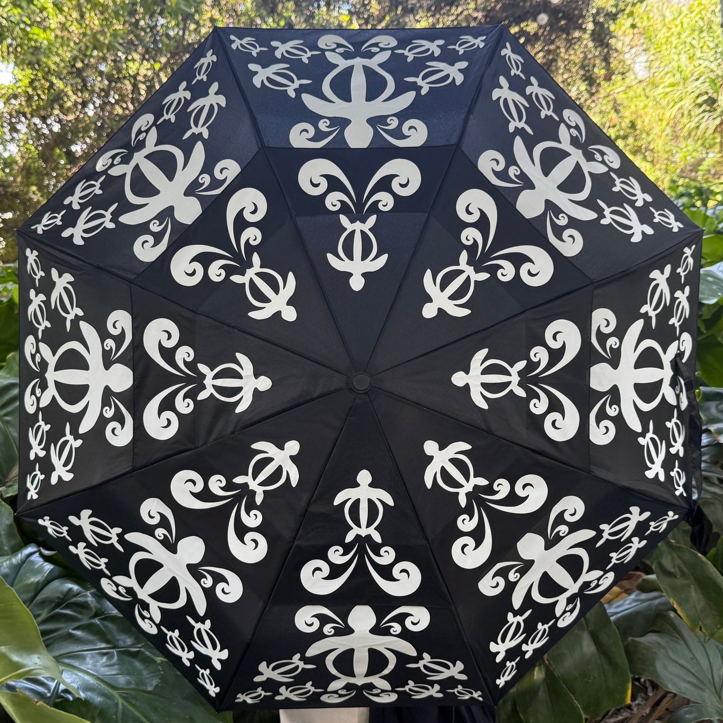 Black umbrella with white patterns held up against a green leafy background