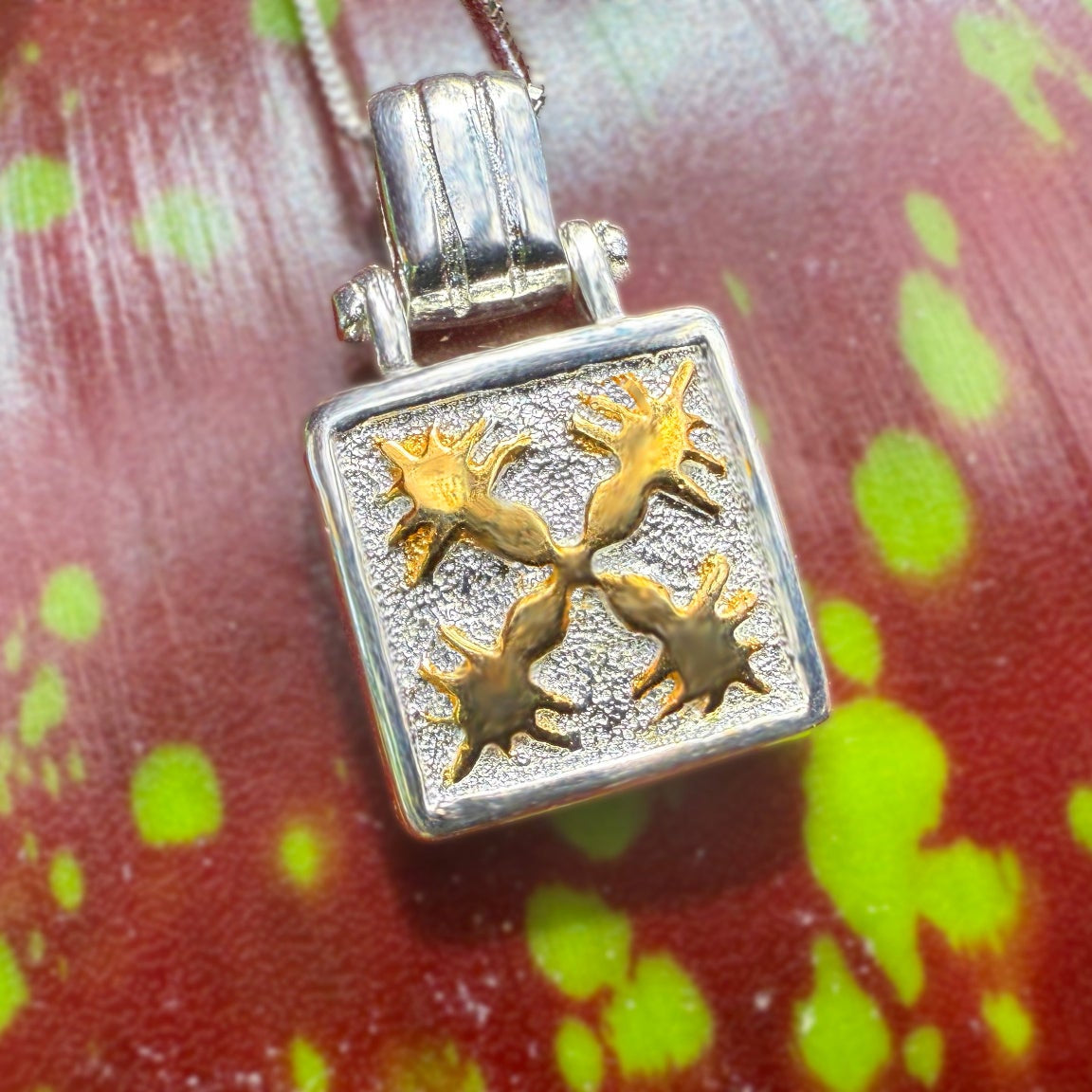 Silver and gold pendant on a red and green leaf