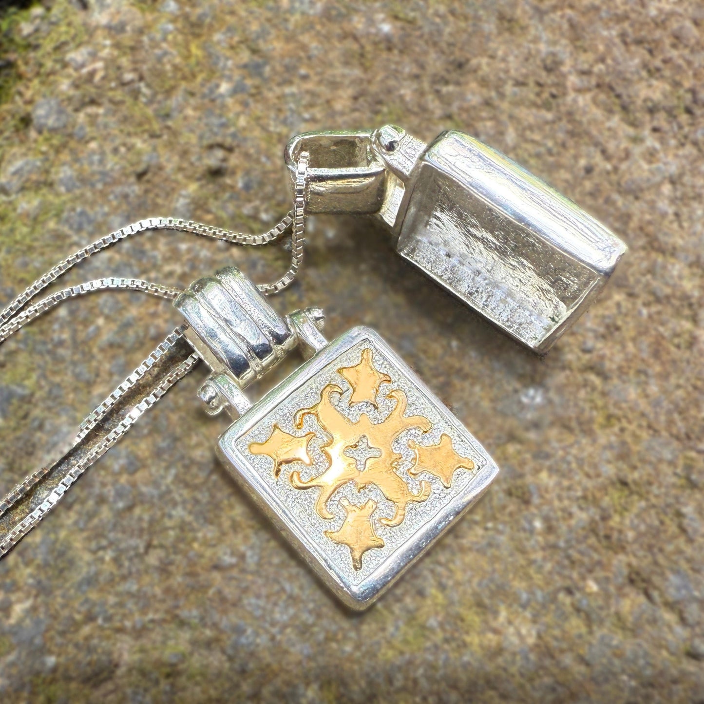 Silver necklace with a pendant featuring gold designs on a stone surface.
