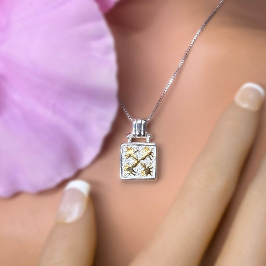 Silver necklace with a square pendant held by a hand against a blurred background