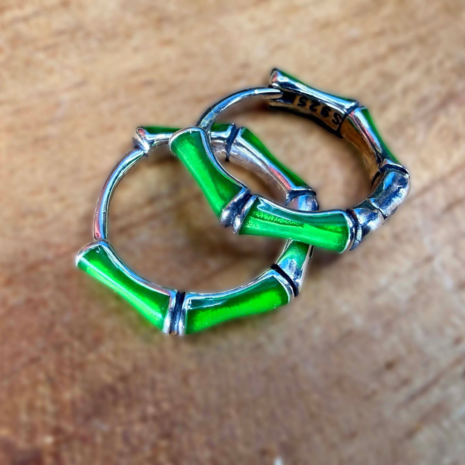 A pair of silver ear rings designed to look like green bamboo stalks with silver bands, resting on a wooden surface.