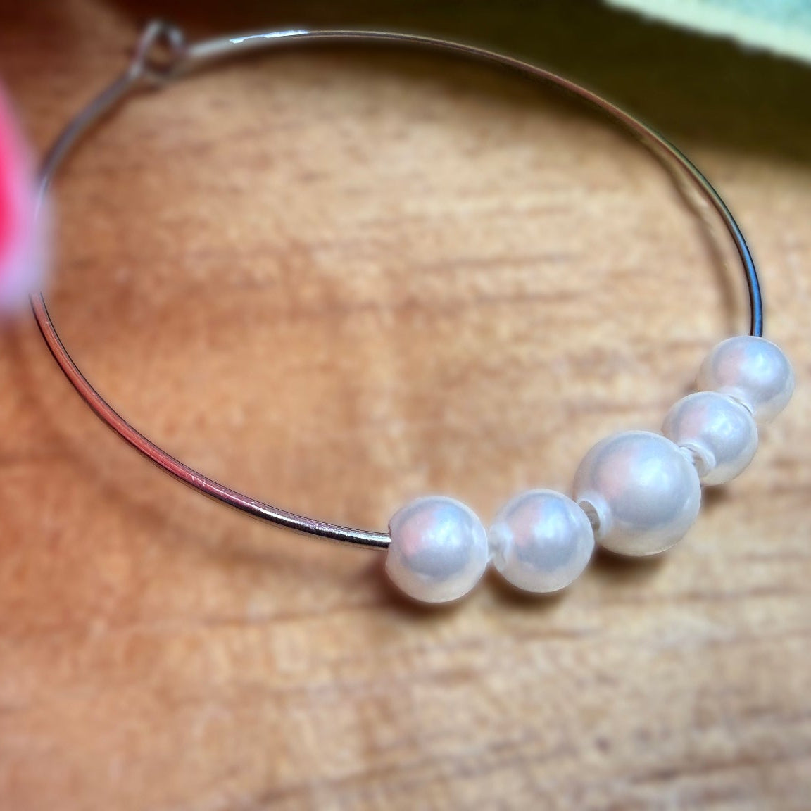 A close-up of a thin silver hoop earring adorned with five white pearl beads, resting on a wooden surface.