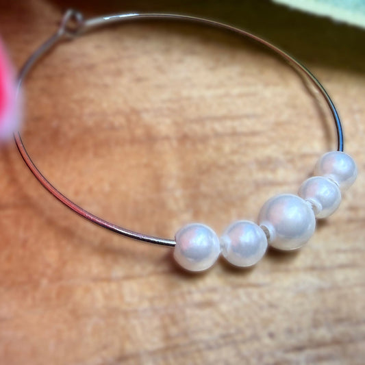 A close-up of a thin silver hoop earring adorned with five white pearl beads, resting on a wooden surface.