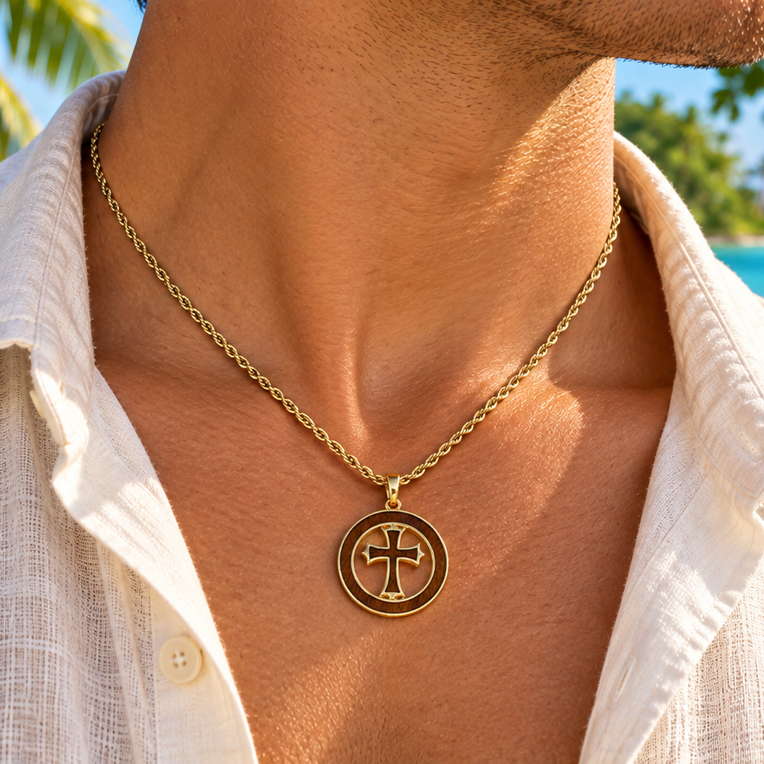 A close-up lifestyle shot of a man wearing a gold chain necklace with a circular pendant featuring a cross, set against a tropical beach background with palm trees and turquoise water.