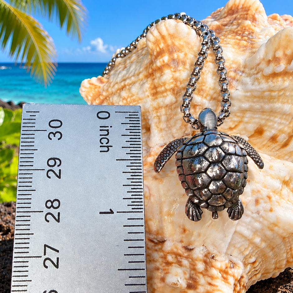 A silver turtle pendant necklace displayed on a large seashell with a metal ruler showing 0 to 10 inches for scale, set against a tropical beach background with palm trees, blue ocean, and a red hibiscus flower.