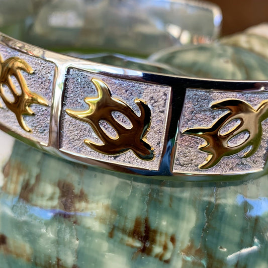 Extreme close up of petroglyph honu cuff with gold honus on a pebble design background with a mirrored sterling silver base.